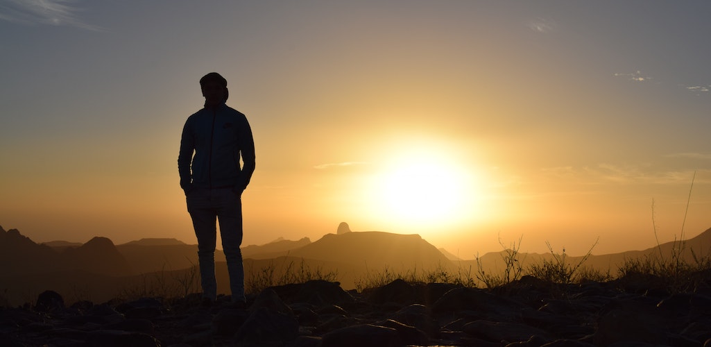 A man standing on a hill backlit by a sunrise