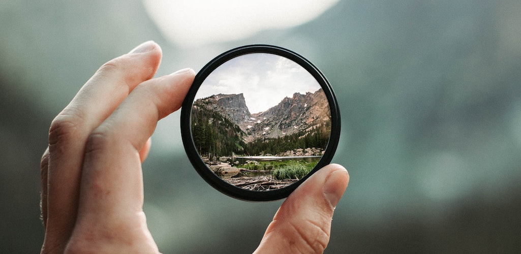 Hand holding a lens with a mountain scene beyond