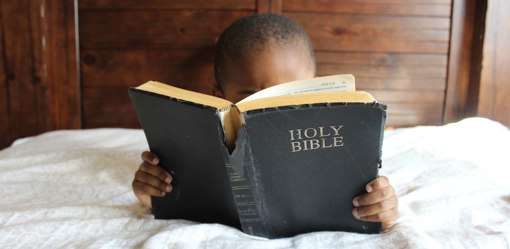 Child reading a Bible on a bed