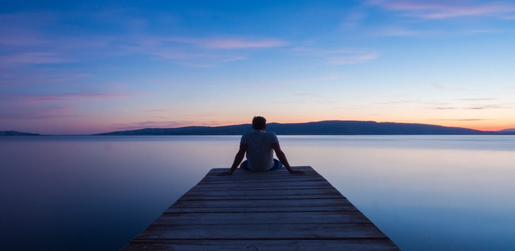 Man sitting on the end of a dock looking at a sunset