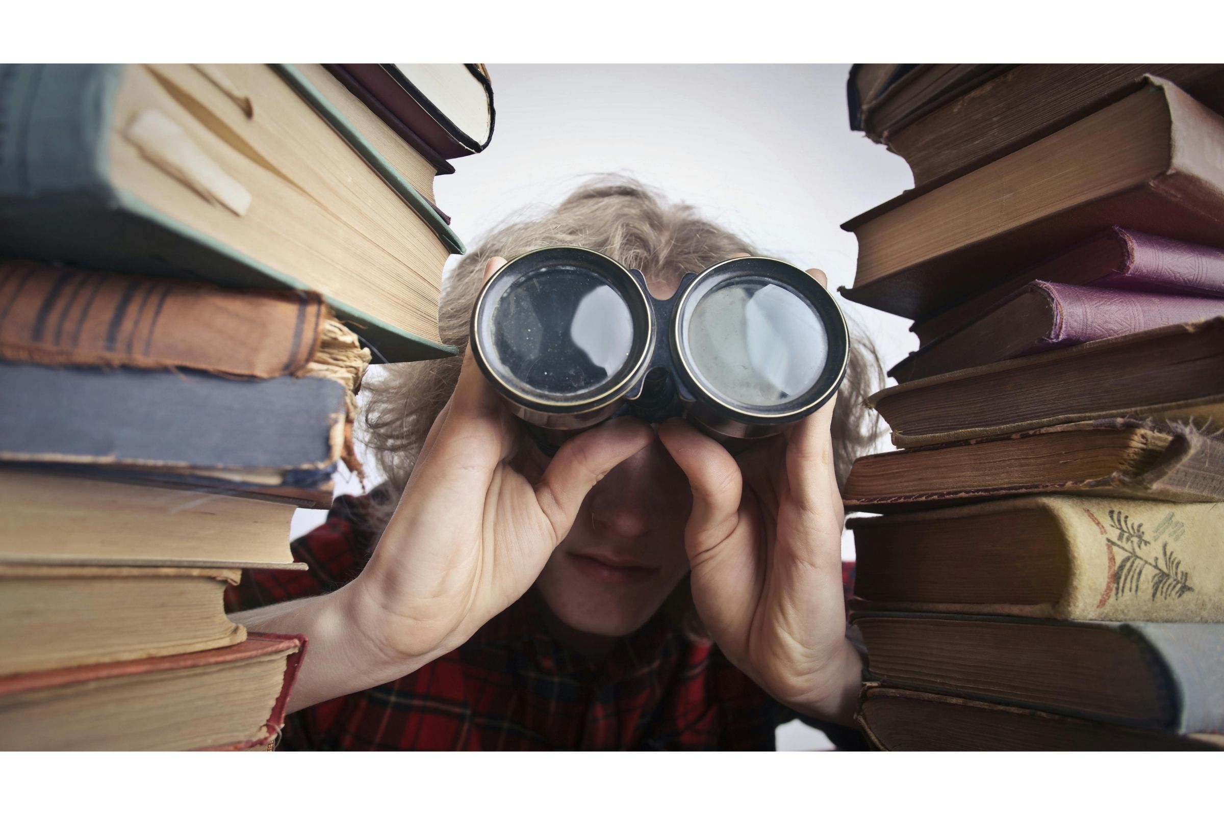 Person peeking through two stacks of books with binocoulars