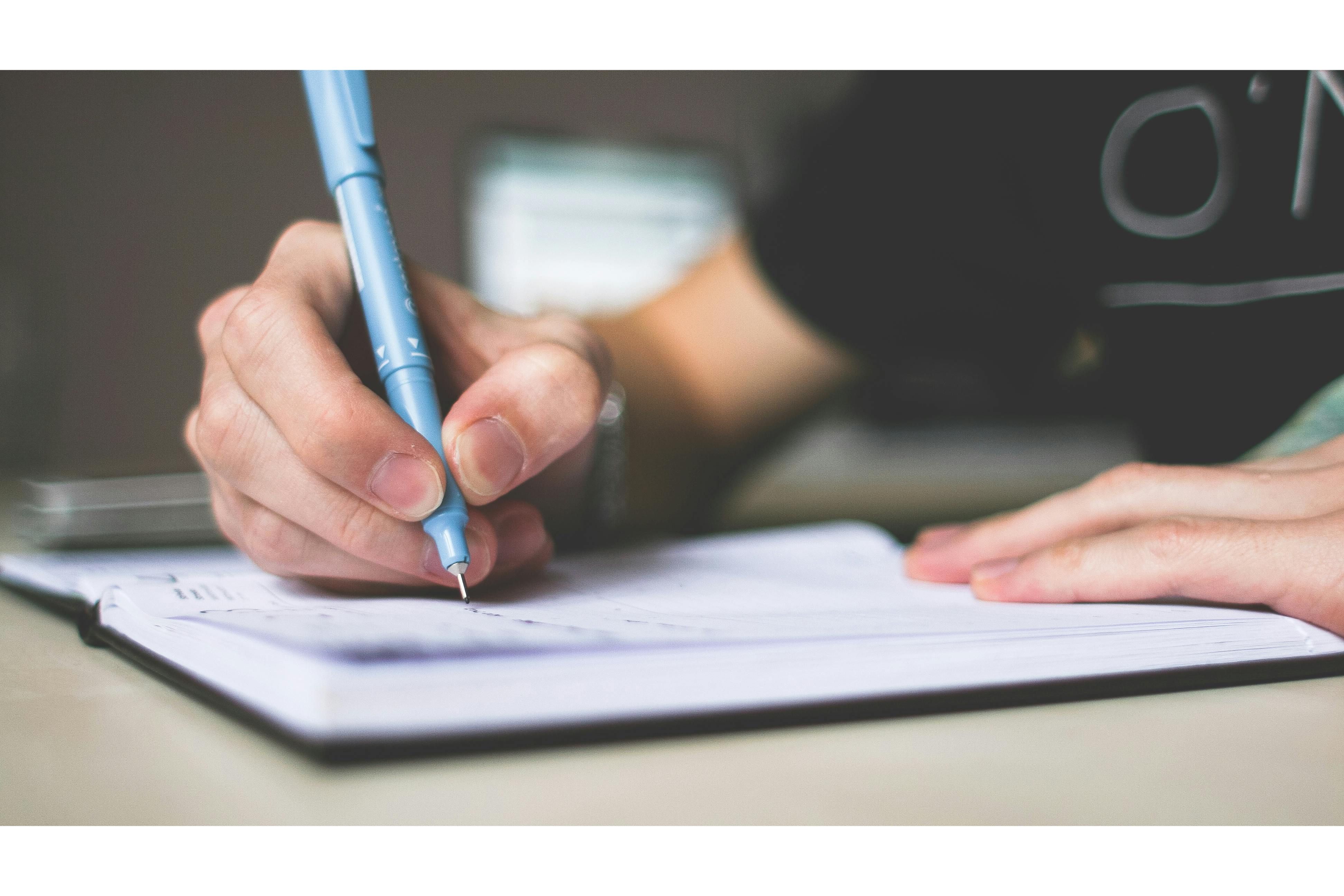 Person writing with a pen in a notebook
