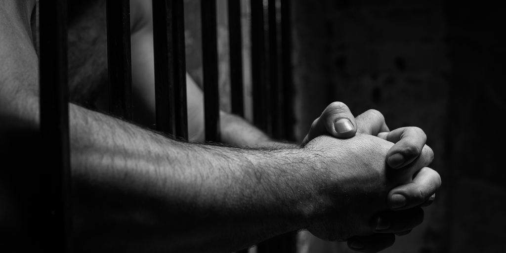Hands folded through jail bars