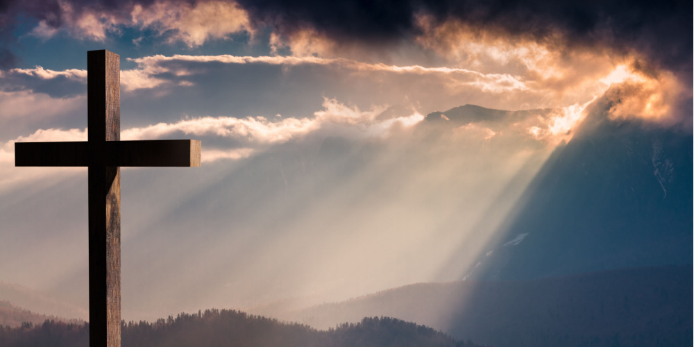 A wooden cross in front of sunbeams shining through dark clouds