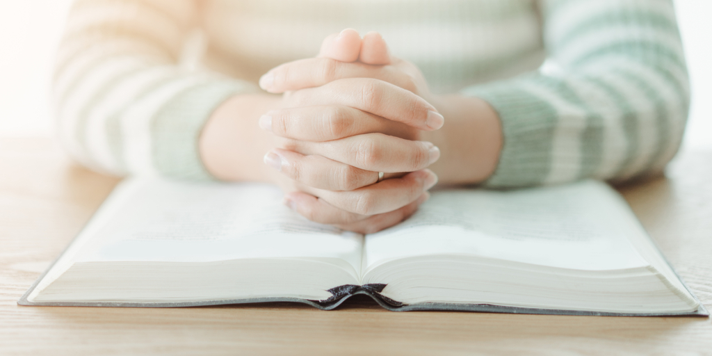 Hands folded on top of a Bible 